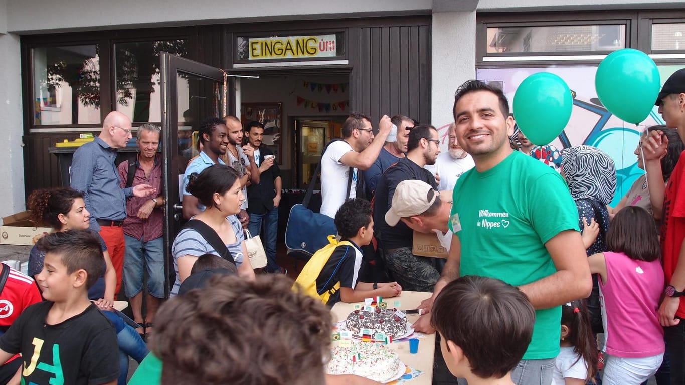 Menschen feiern mit Kuchen und Luftballons vor einem Gebäude: Fest zum zweijährigen Bestehen des benachbarten "Café international“.