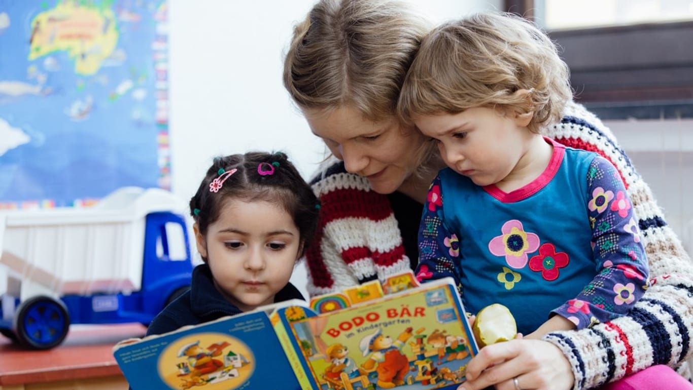 Eine Frau liest zwei kleinen Kindern aus einem Buch vor: Betreuung der Flüchtlingskinder im WiN-Haus.