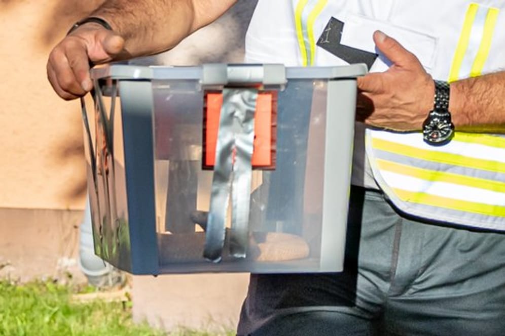 Ein Reptilienexperte trägt die eingefangene Monokelkobra in einem Behälter aus einem Hauseingang.