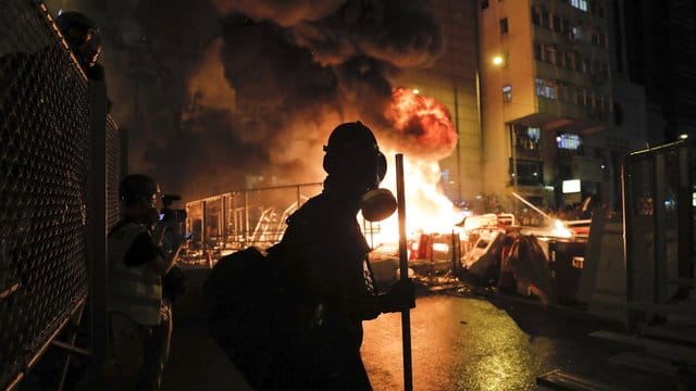 Ein Demonstrant mit einer Gasmaske steht vor den lodernden Flammen eines Feuers in Hongkong. Ein Demonstrant mit einer Gasmaske steht vor den lodernden Flammen eines Feuers in Hongkong.