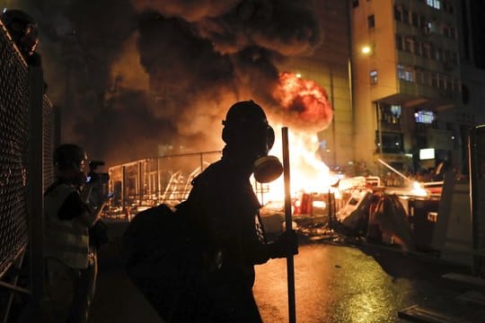 Ein Demonstrant mit einer Gasmaske steht vor den lodernden Flammen eines Feuers in Hongkong.
