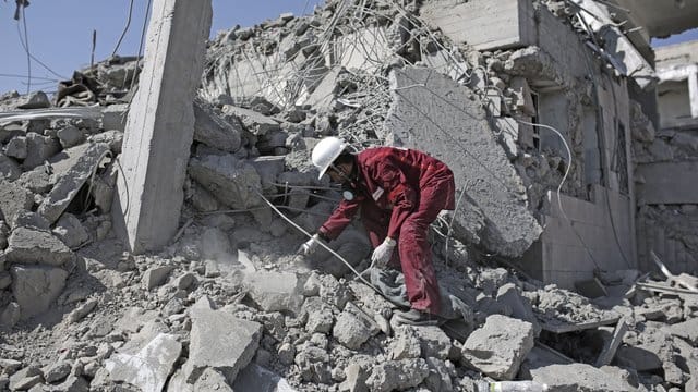 Eine Rettungskraft sucht in den Trümmern eines Gefangenenlagers nach verschütteten Leichen. Eine Rettungskraft sucht in den Trümmern eines Gefangenenlagers nach verschütteten Leichen.