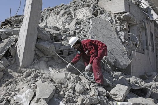 Eine Rettungskraft sucht in den Trümmern eines Gefangenenlagers nach verschütteten Leichen.