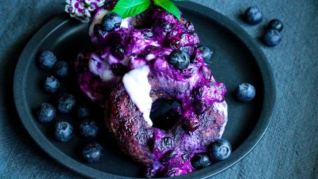 Die Donuts werden am Ende der Backzeit im Saft der Heidelbeeren gewendet und dann mit Joghurt serviert.