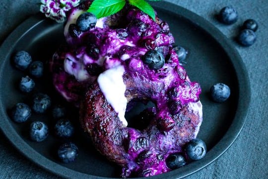 Die Donuts werden am Ende der Backzeit im Saft der Heidelbeeren gewendet und dann mit Joghurt serviert.