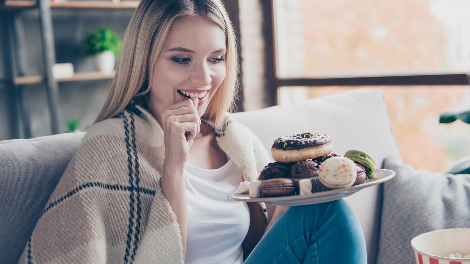 Eine Frau sitzt mit Kuchen auf dem Sofa: Am Cheat Day kann die hohe Zuckerzufuhr zu einer starken Erhöhung des Blutzuckerspiegels führen.