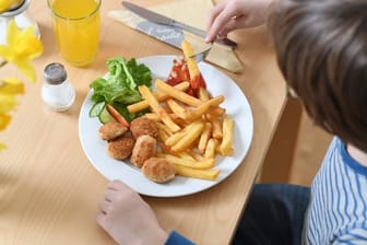 Ein Junge sitzt vor einem Teller mit Chicken Nuggets und Pommes Frites (Archiv).