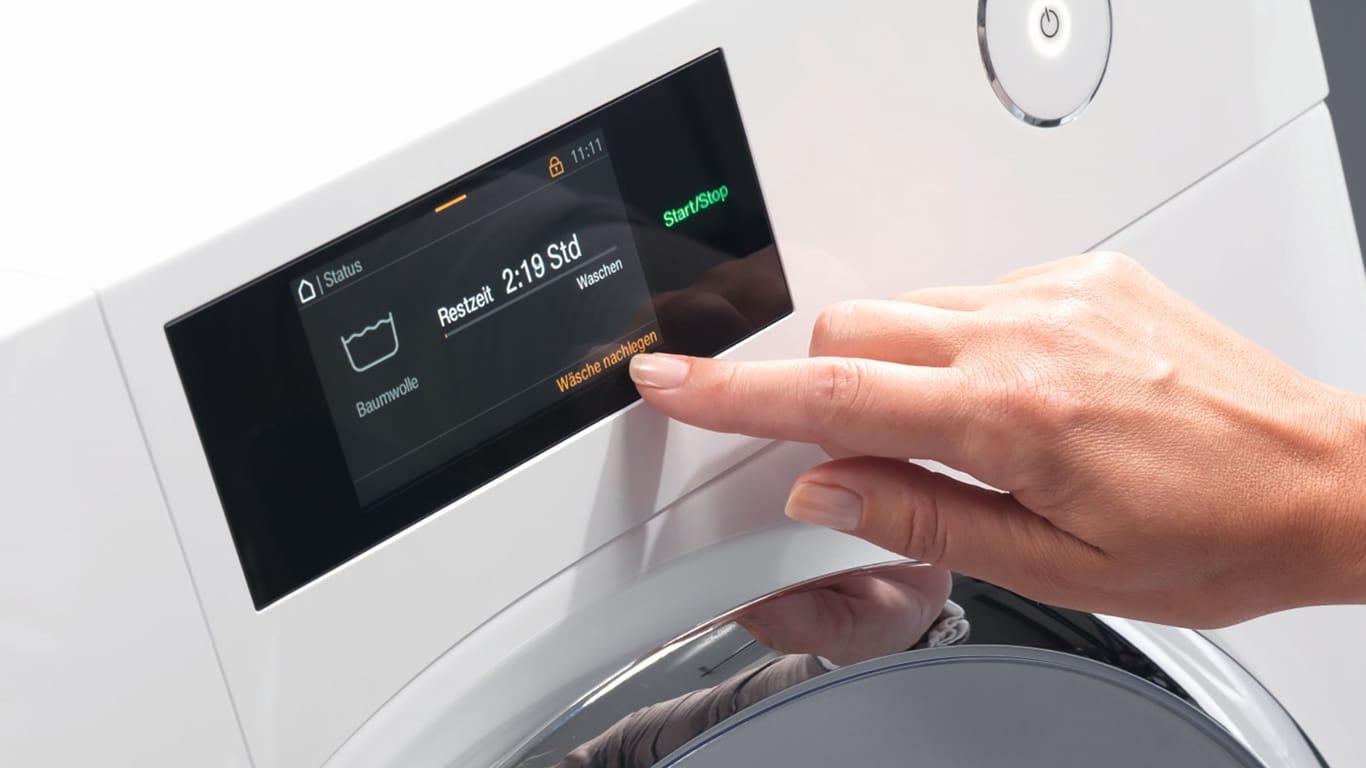 Eine Frau bedient eine smarte Waschmaschine: Mieles neue Waschmaschinen lassen sich künftig im laufenden Betrieb auf Pause stellen, um vergessene Kleidungsstücke nachzulegen.