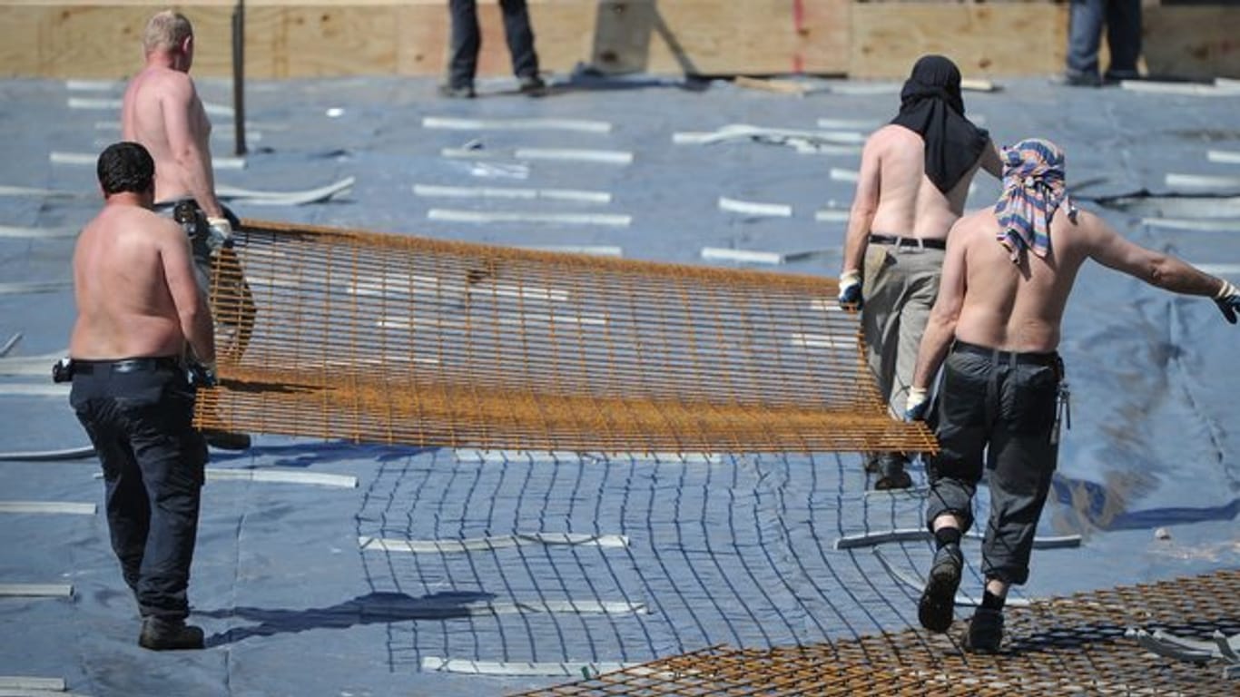 Arbeiter mit freiem Oberkörper tragen auf einer Baustelle ein Stahlgitter.