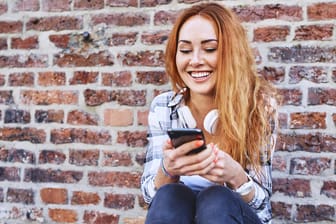 Eine junge Frau nutzt ihr Smartphone: Viele Nutzer schrecken davor zurück, ein gebrauchtes Smartphone zu kaufen. Dabei lässt sich dabei viel Geld sparen.