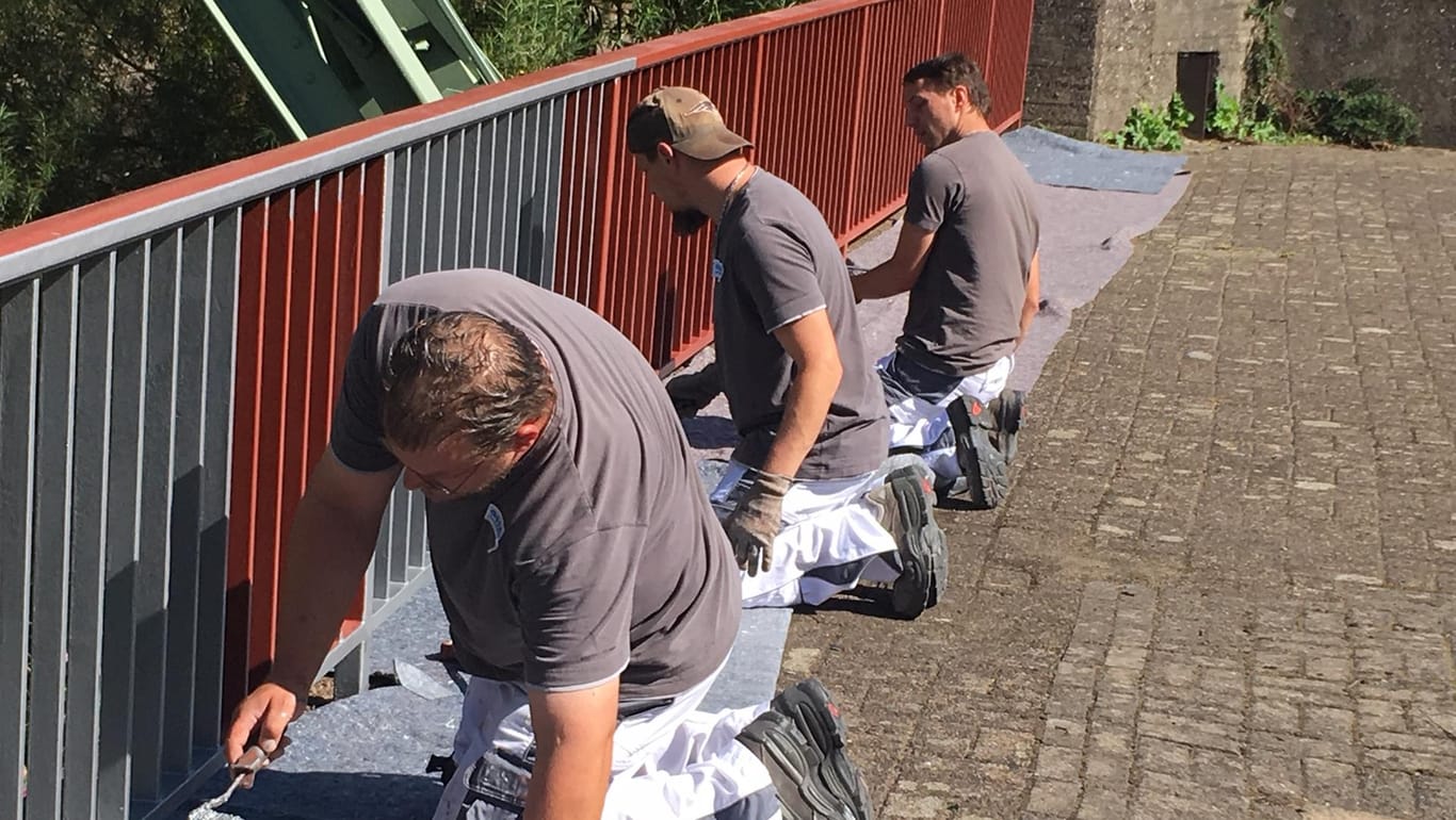 Drei Männer streichen ein Geländer an: Die Azubis bei der Arbeit am Projekt "Ufer".