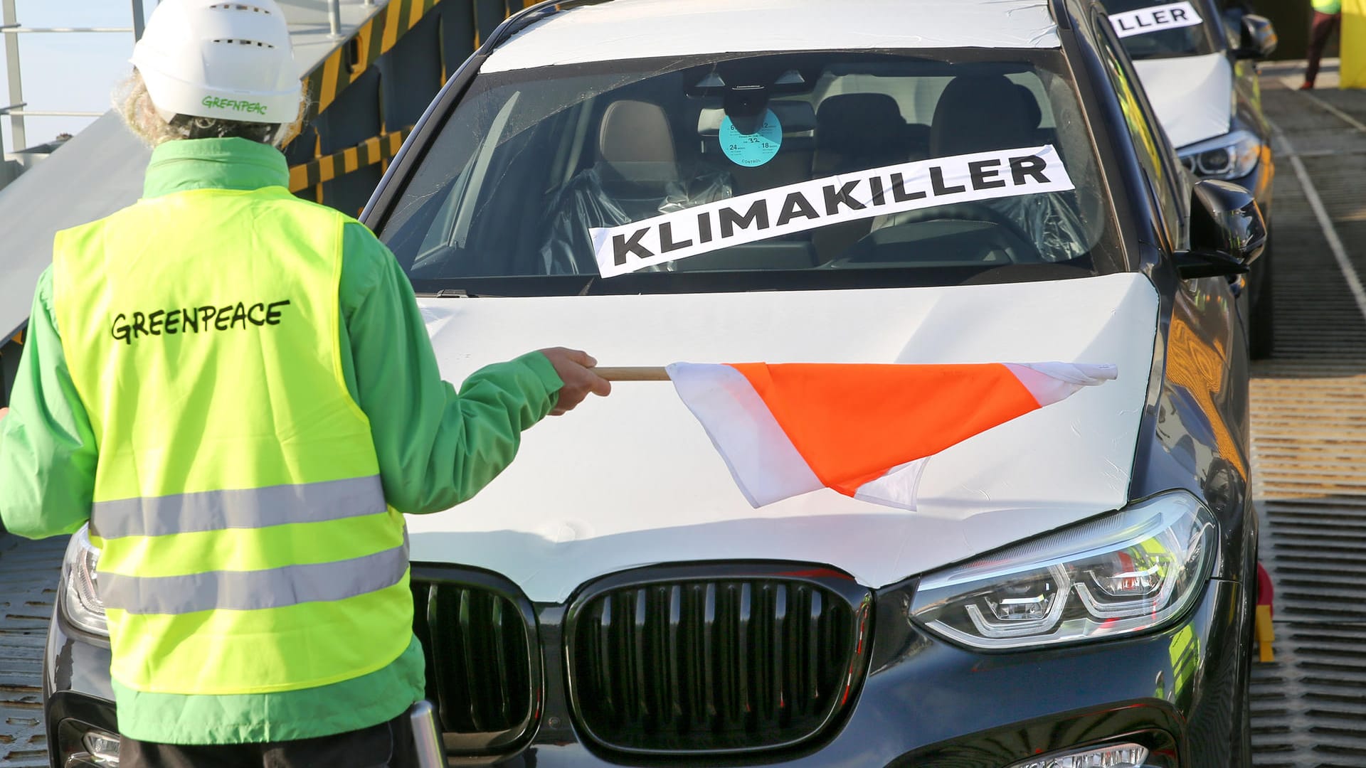 Greenpeace-Aktivist vor einem SUV: Die Demonstranten blockieren das Entladen von SUV-Fahrzeugen. Die rasante Zunahme an SUVs gefährde Klimaziele im Verkehr und gefährde andere Verkehrsteilnehmende im Straßenverkehr.