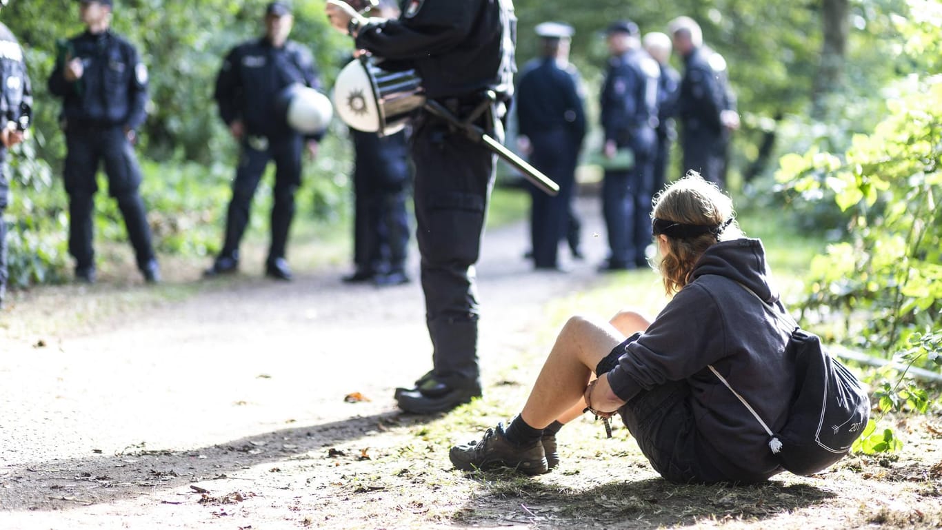 Ein Mann sitzt vor Einsatzkräften: In Hamburg-Wilhelmsburg haben Aktivisten einen Wald besetzt.