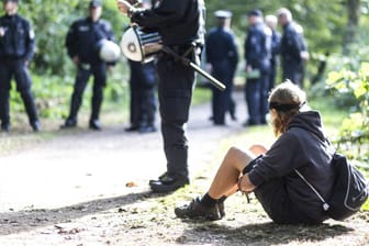 Ein Mann sitzt vor Einsatzkräften: In Hamburg-Wilhelmsburg haben Aktivisten einen Wald besetzt.