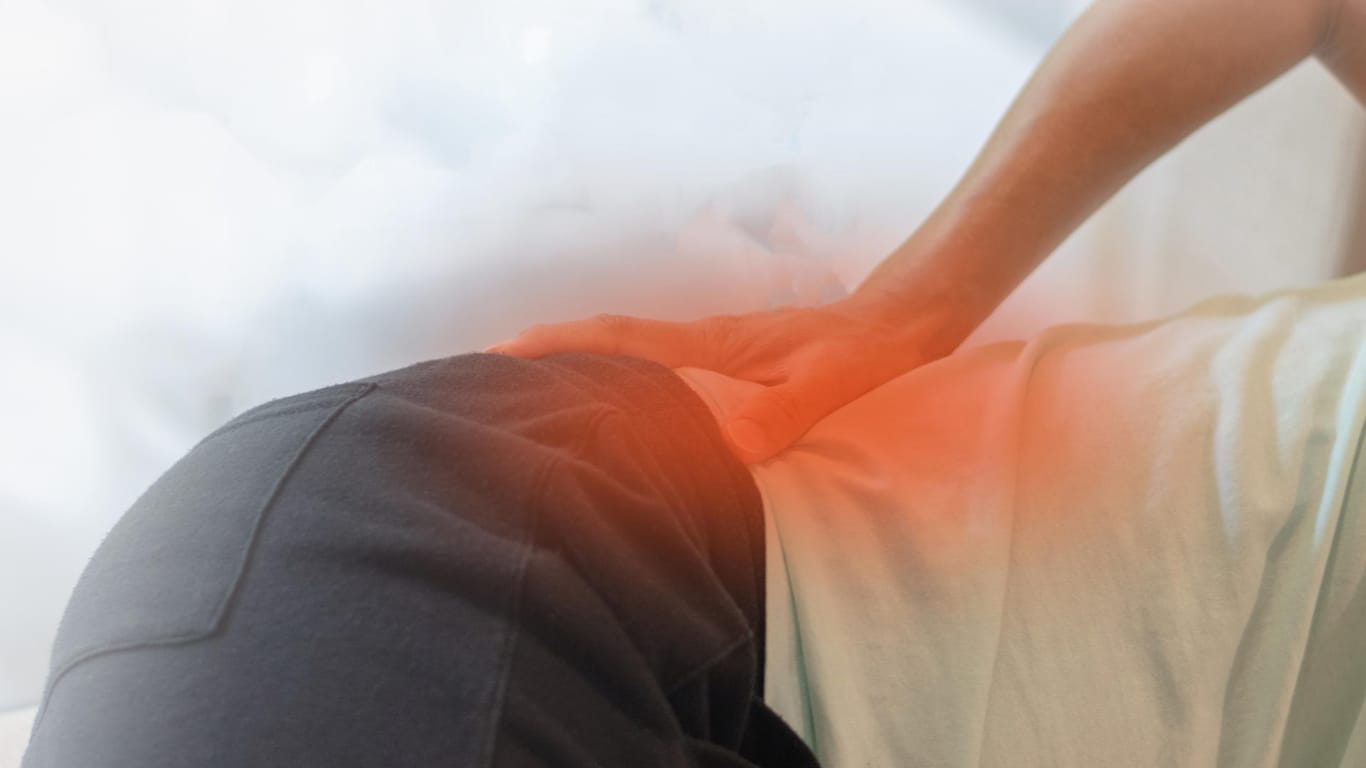 Patient mit Schmerzen in der Hüfte: Ein lang anhaltender und tief sitzender Rückenschmerz ist ein typisches Symptom von Morbus Bechterew.