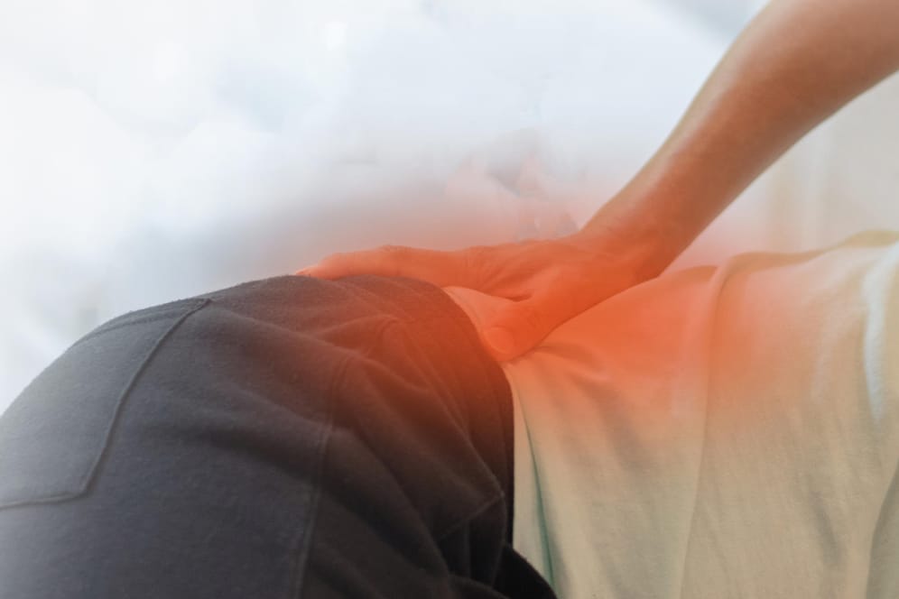 Patient mit Schmerzen in der Hüfte: Ein lang anhaltender und tief sitzender Rückenschmerz ist ein typisches Symptom von Morbus Bechterew.