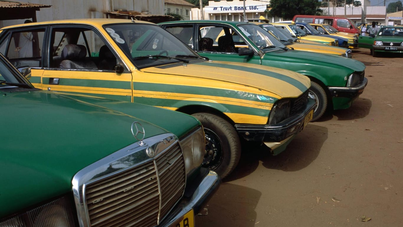 Taxistand in Gambia: Weil es in Gambia kein funktionierendes Bus- und Bahnsystem gibt, wählen viele Menschen die charakteristischen grün-gelben Taxis, um von einem Ort zum anderen zu gelangen.