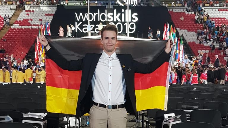 Ein Mann steht mit einer Deutschlandfahne in einer Halle: Der 19-Jährige ist ein wahres Talent im Programmieren.