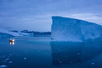 Ein Boot umfährt in der Dämmerung einen Eisberg in Grönland: Nicht nur die Luft lässt das Eis schmelzen – sondern auch das Meerwasser. (Archivbild)