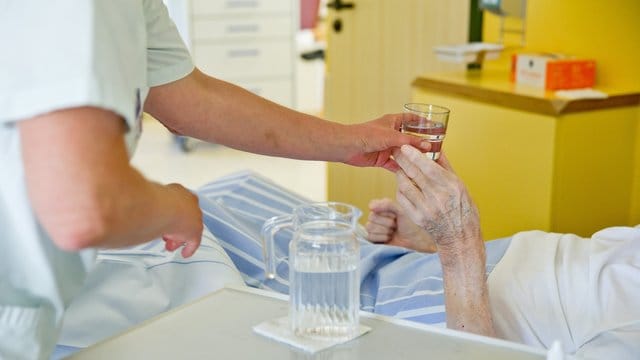 Eine Krankenpflegerin reicht einem Patienten in einem Klinikum ein Glas Wasser.