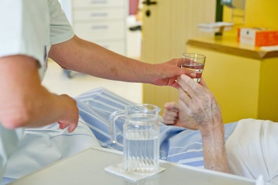 Eine Krankenpflegerin reicht einem Patienten in einem Klinikum ein Glas Wasser.