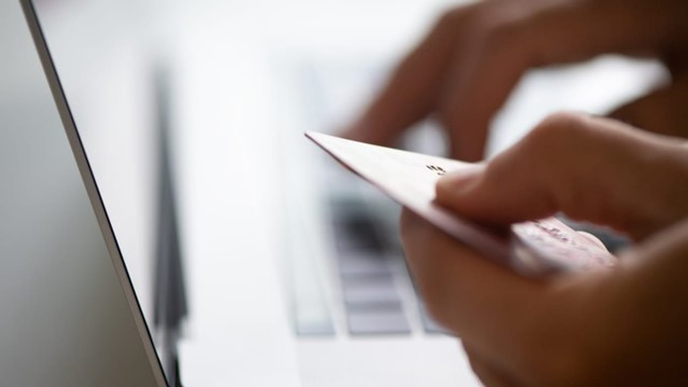Ein Nutzer an einem Laptop mit Kreditkarte in der Hand: Neue Regeln sollen Online-Shopping künftig sicherer machen.