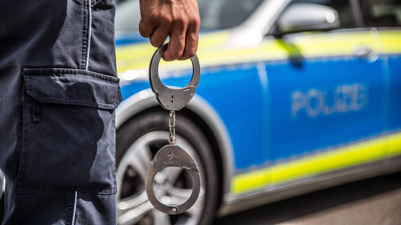Ein Polizist steht mit Handschellen vor einem Streifenwagen: Durch eine Schulfahndung konnte ein Mann identifiziert werden, der seine Nichte mehrfach sexuell missbraucht haben soll.