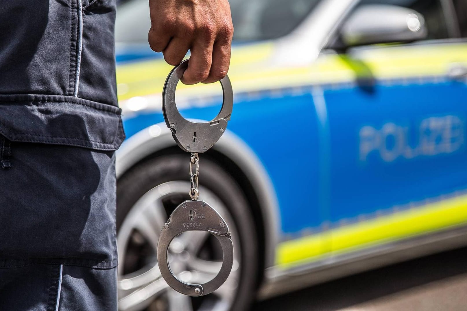 Ein Polizist steht mit Handschellen vor einem Streifenwagen: Durch eine Schulfahndung konnte ein Mann identifiziert werden, der seine Nichte mehrfach sexuell missbraucht haben soll.
