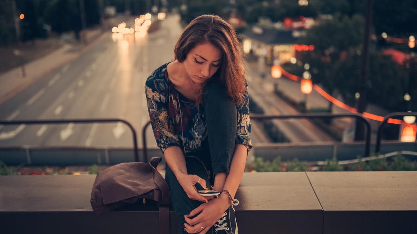 Junge Frau blickt auf ihr Handy: In der Freizeit fühlen sich viele Deutsche gestresst.