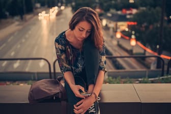 Junge Frau blickt auf ihr Handy: In der Freizeit fühlen sich viele Deutsche gestresst.