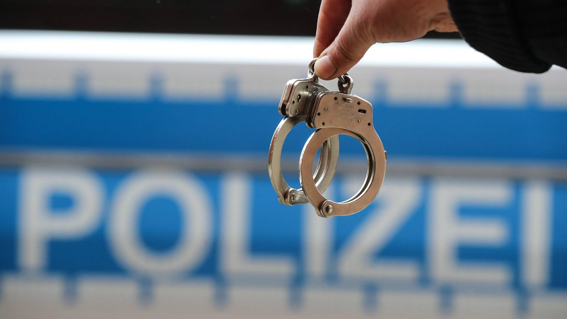 Handschellen vor einem Polizeiauto: Die falschen Beamten sitzen jetzt in Untersuchungshaft – die Polizei geht von Bandenkriminalität aus.