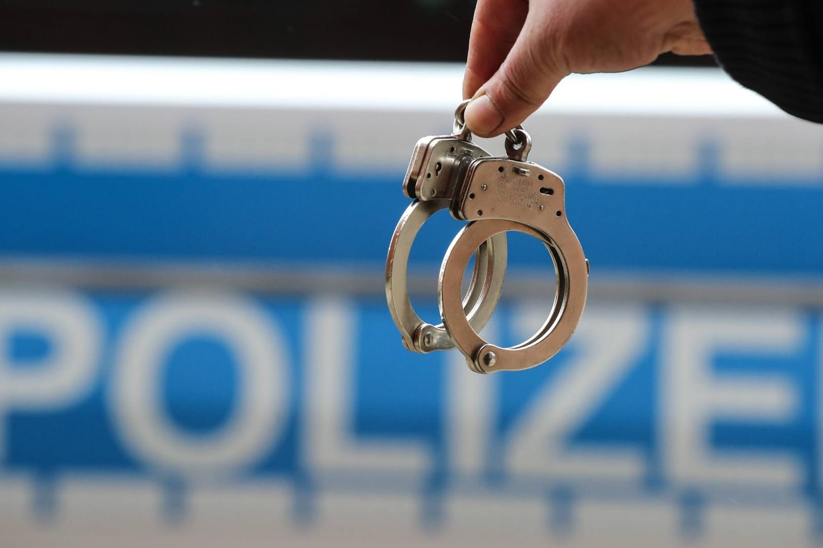 Handschellen vor einem Polizeiauto: Die falschen Beamten sitzen jetzt in Untersuchungshaft – die Polizei geht von Bandenkriminalität aus.