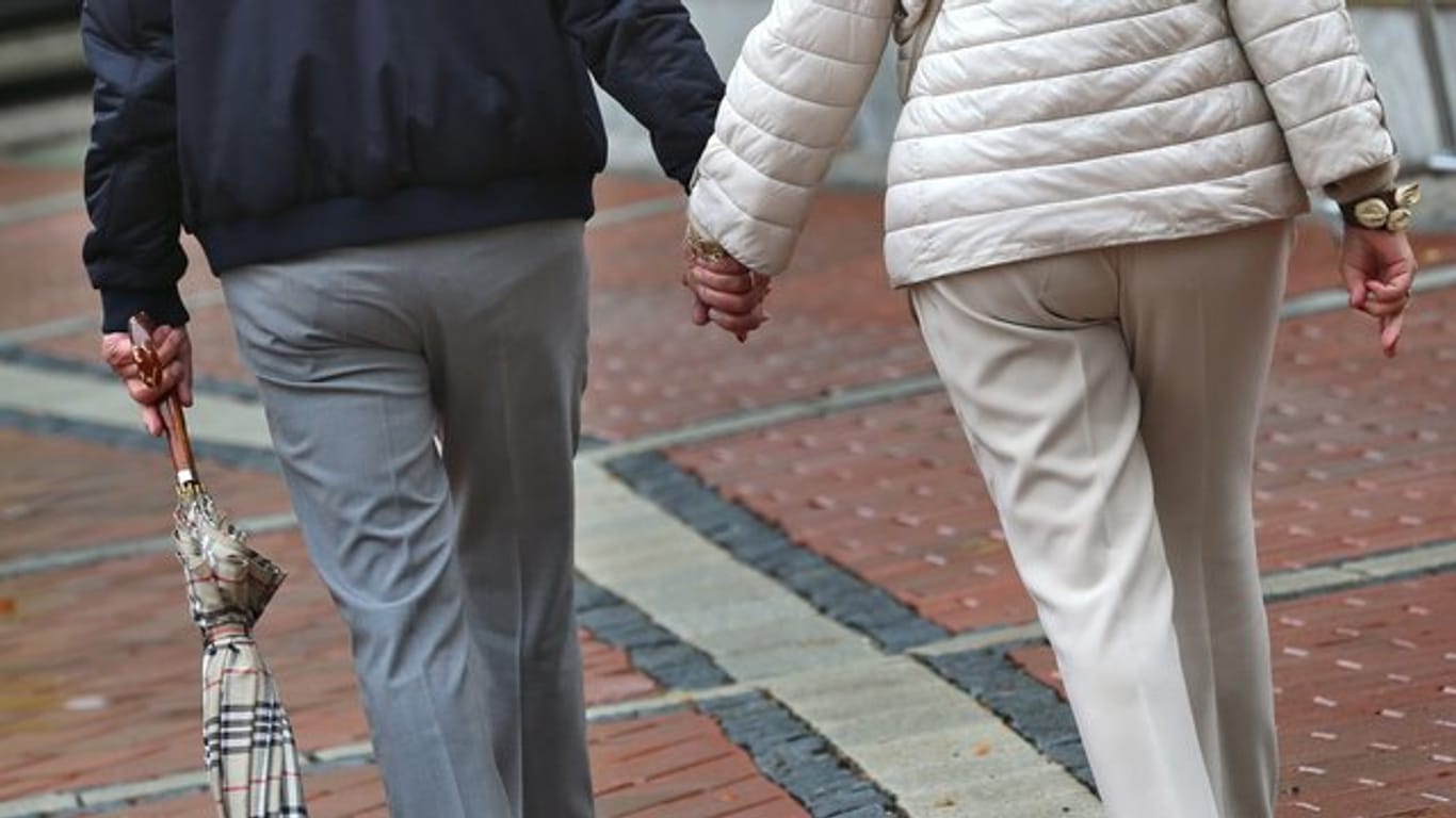 Ein älteres Paar Hand in Hand in einer Fußgängerzone.