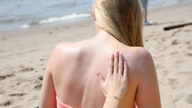 Eine junge Frau wird am Strand mit Sonnencreme eingerieben.