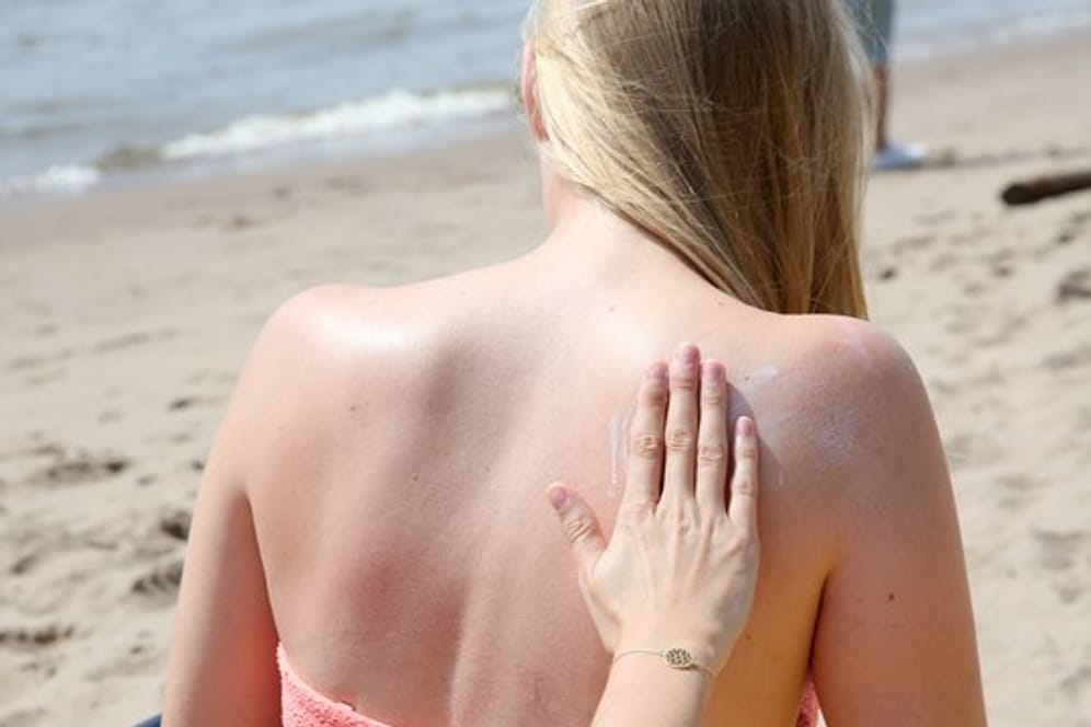 Eine junge Frau wird am Strand mit Sonnencreme eingerieben.