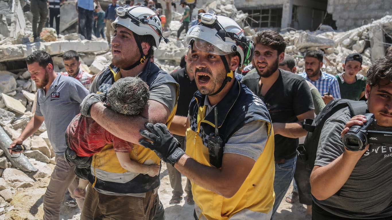 Syrien, Maarat al-Numan: Weißhelme des syrischen Zivilschutzes tragen ein verletztes Kind aus den Trümmern eines zerstörten Gebäudes.
