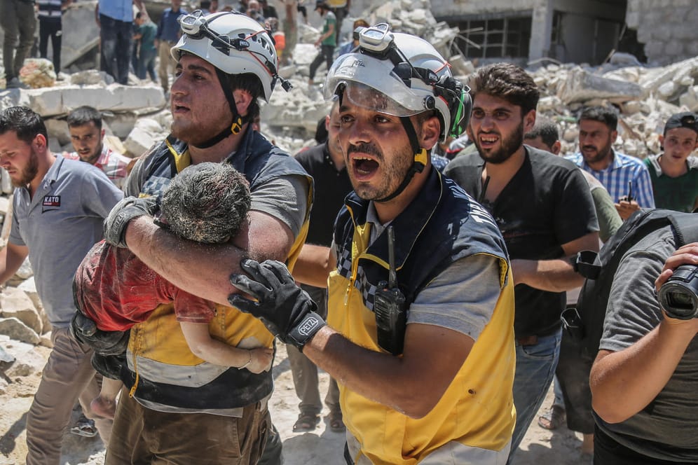 Syrien, Maarat al-Numan: Weißhelme des syrischen Zivilschutzes tragen ein verletztes Kind aus den Trümmern eines zerstörten Gebäudes.
