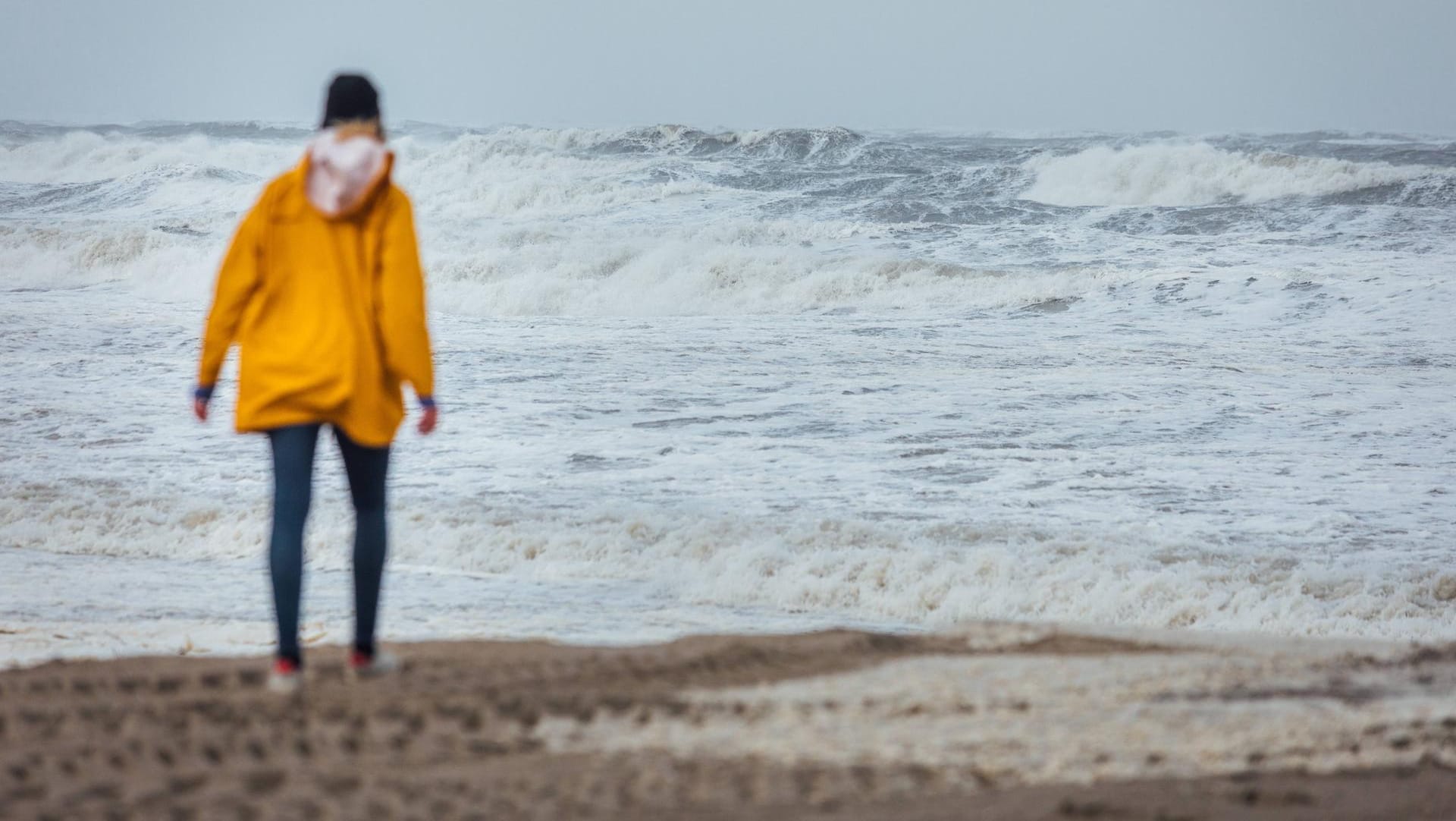 Ein Spaziergängerin in Regenjacke an der Küste: An Nord- und Ostsee ist mit schweren Sturmböen mit bis zu 100 Kilometern pro Stunde zu rechnen. (Symbolbild)