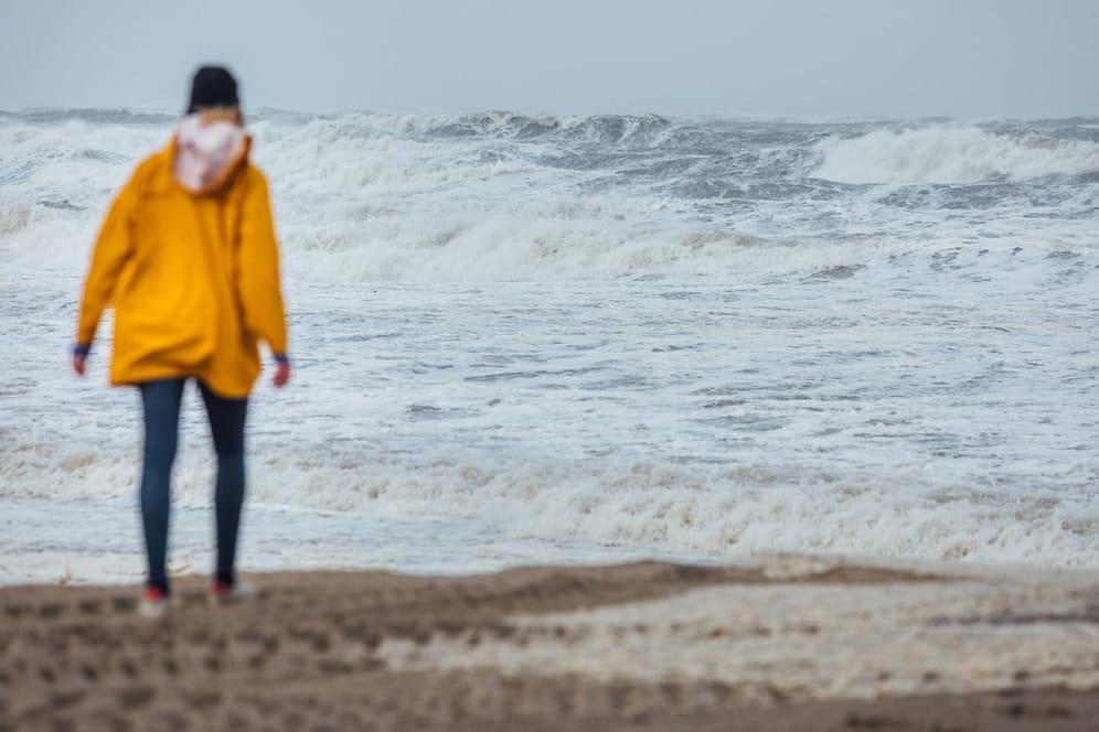 Ein Spaziergängerin in Regenjacke an der Küste: An Nord- und Ostsee ist mit schweren Sturmböen mit bis zu 100 Kilometern pro Stunde zu rechnen. (Symbolbild)