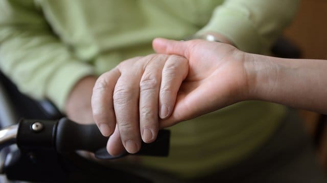 Eine junge Frau hält die Hände eines alten Mannes.