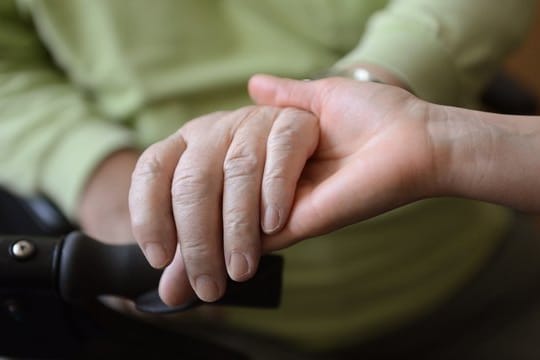 Eine junge Frau hält die Hände eines alten Mannes.