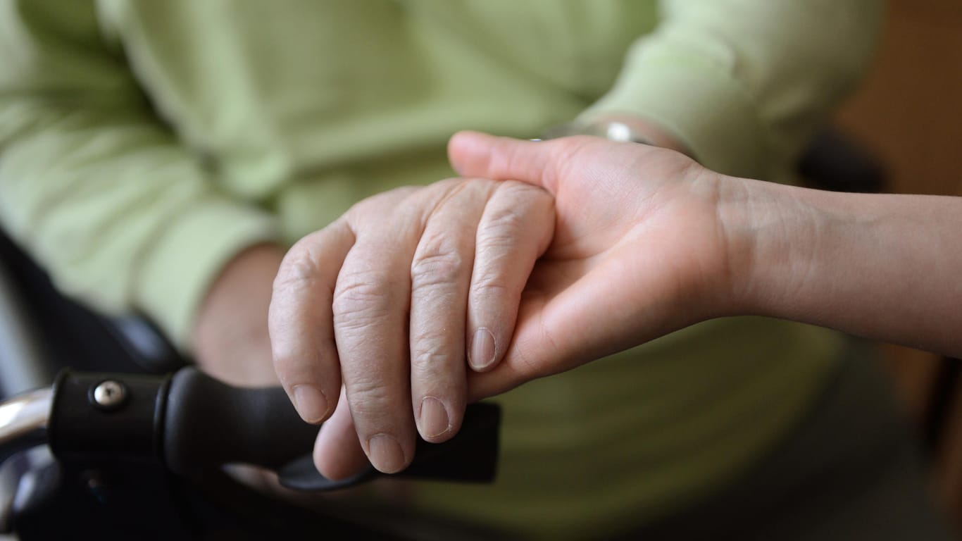 Eine junge Frau hält die Hand eines anderen: Der Pflegegutachter kommt zu einem einzigen vorher angekündigten Termin nach Hause.