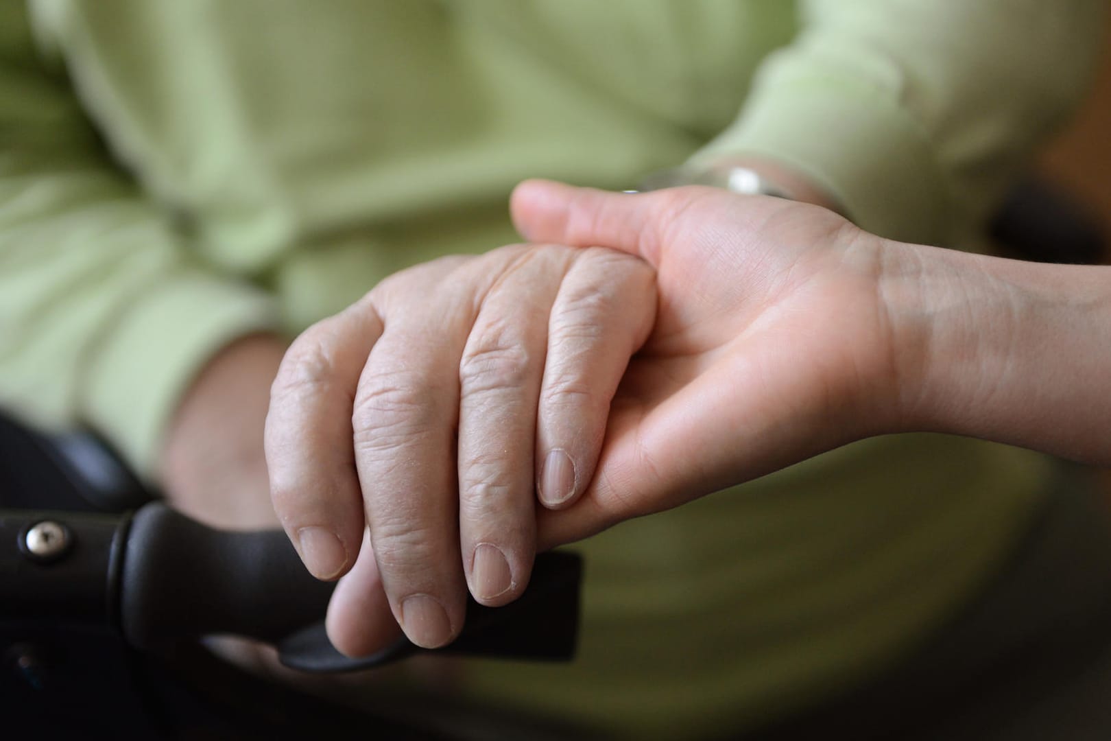 Eine junge Frau hält die Hand eines anderen: Der Pflegegutachter kommt zu einem einzigen vorher angekündigten Termin nach Hause.