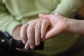 Eine junge Frau hält die Hand eines anderen: Der Pflegegutachter kommt zu einem einzigen vorher angekündigten Termin nach Hause.