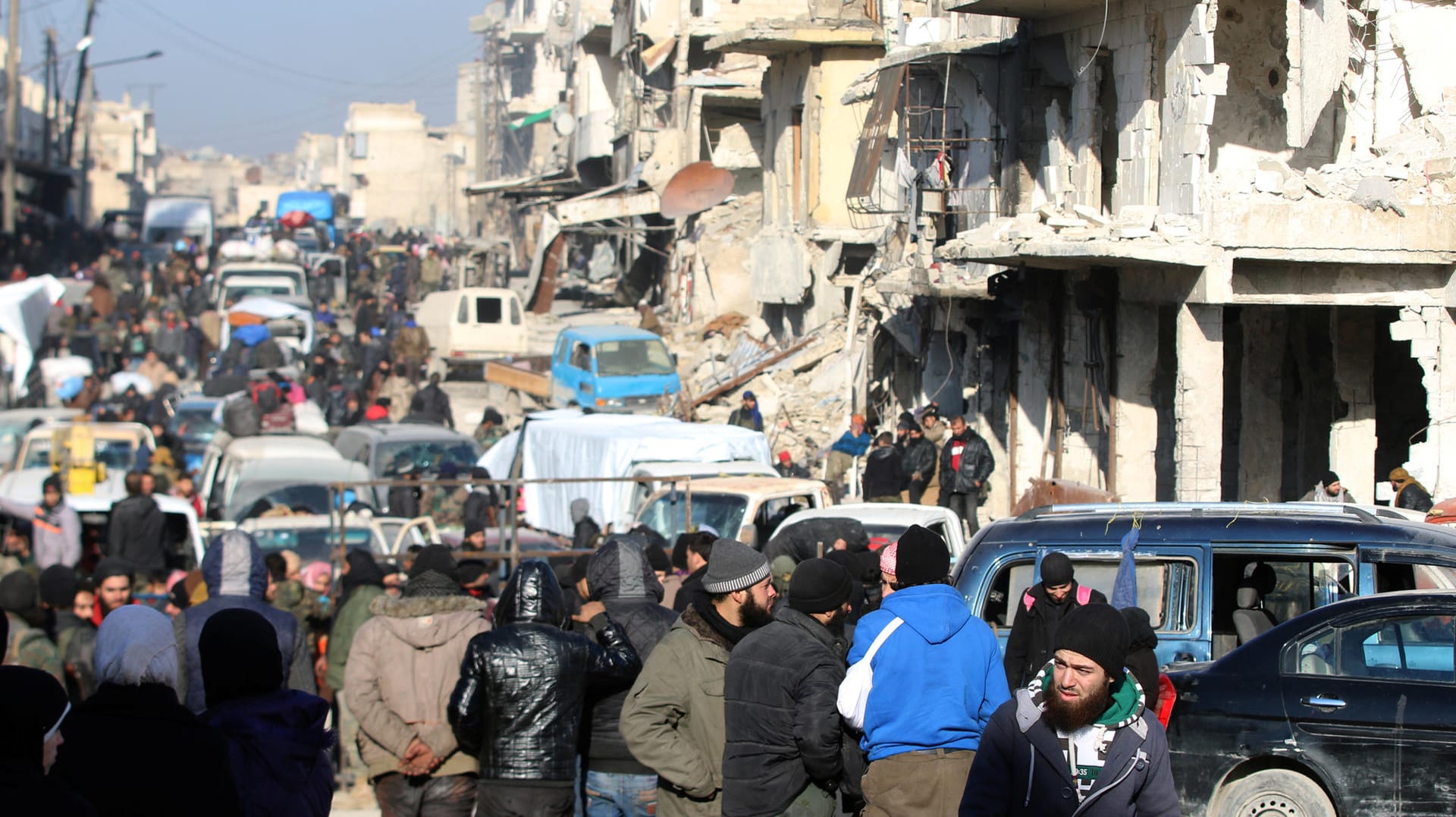 Rebel fighters and civilians wait near damaged buildings to be evacuated from a rebel-held sector of eastern Aleppo