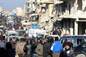 Rebel fighters and civilians wait near damaged buildings to be evacuated from a rebel-held sector of eastern Aleppo
