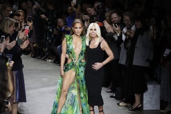 Die Schauspielerin und Tänzerin Jennifer Lopez (l) und die italienische Designerin Donatella Versace nehmen nach der Modenschau den Applaus des Publikums entgegen.