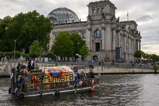 Demonstranten fahren mit einem Boot am Berliner Reichstagsgebäude vorbei.