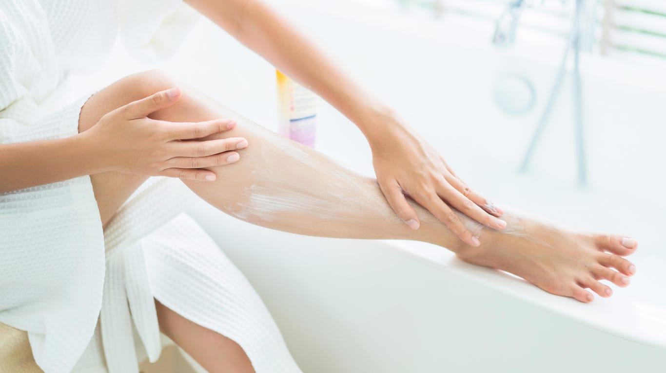 Eine Frau cremt ihren Körper ein: Insbesondere an den Armen und Beinen benötigt die Haut nach dem Duschen und Baden Pflege.