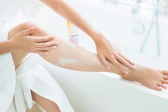 Eine Frau cremt ihren Körper ein: Insbesondere an den Armen und Beinen benötigt die Haut nach dem Duschen und Baden Pflege.